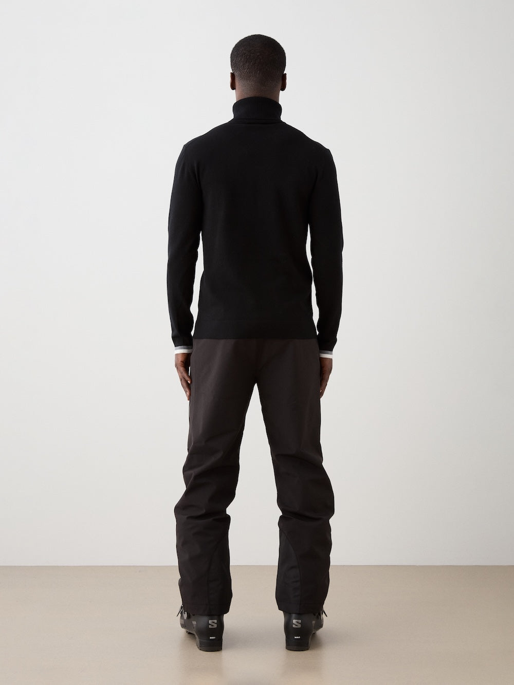 Person wearing black turtleneck and dark pants on a white background
