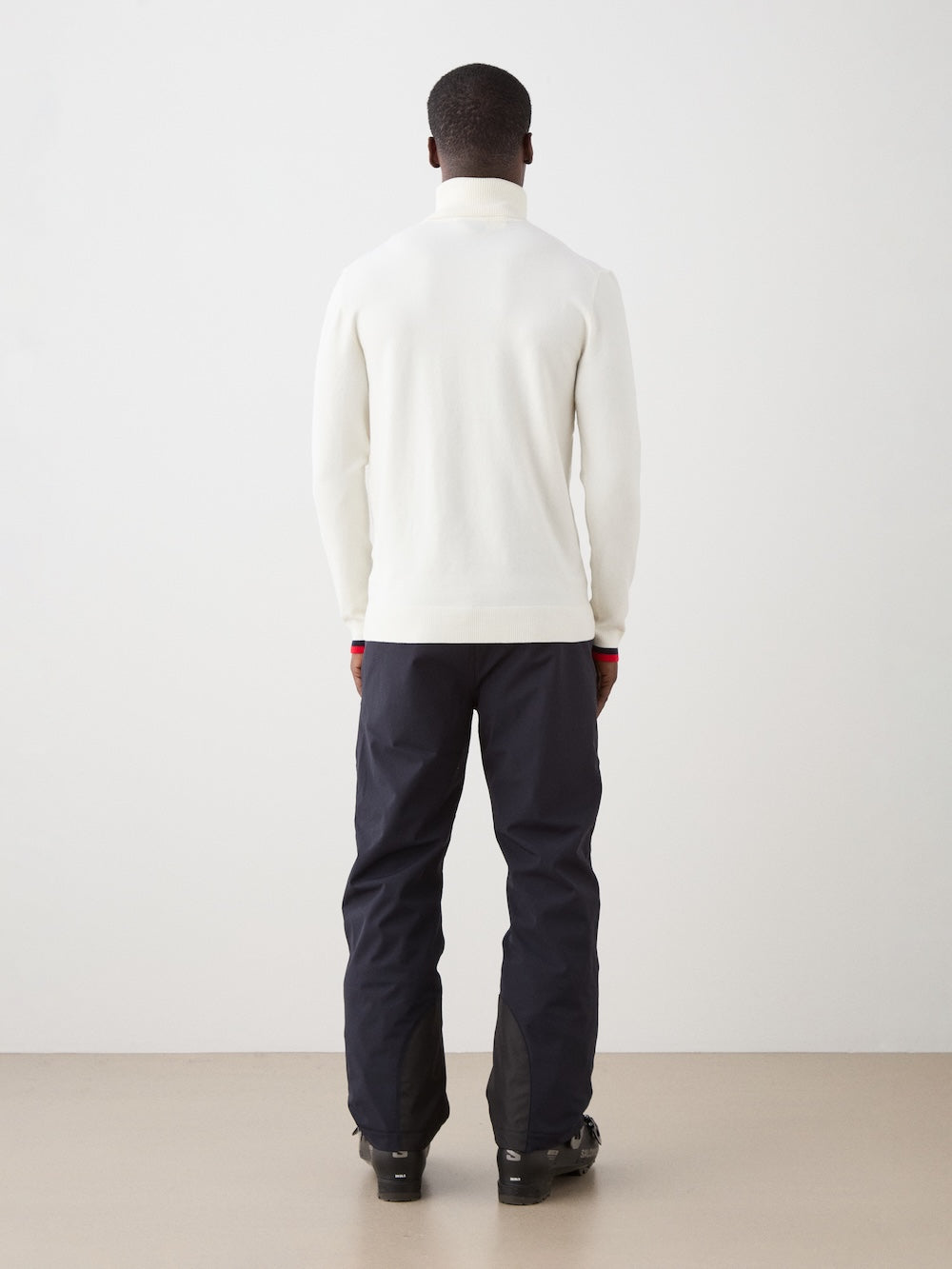Person wearing a white sweater and black pants standing against a white background