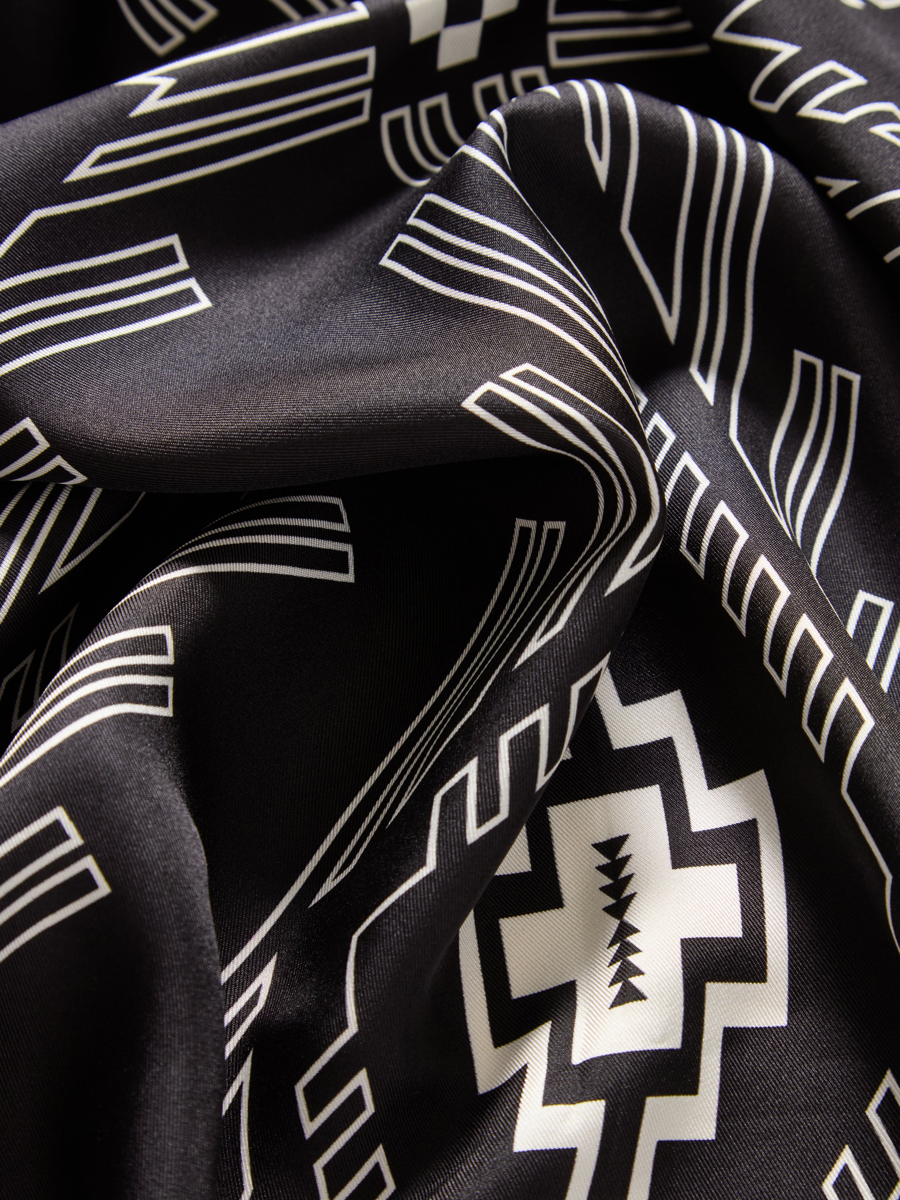 We Norwegians | FW25 | Pioneer Silk scarf_Black | A pure silk scarf printed with motifs inspired by Indigenous Native American art against an off-white background | Picture showing fabric and print details