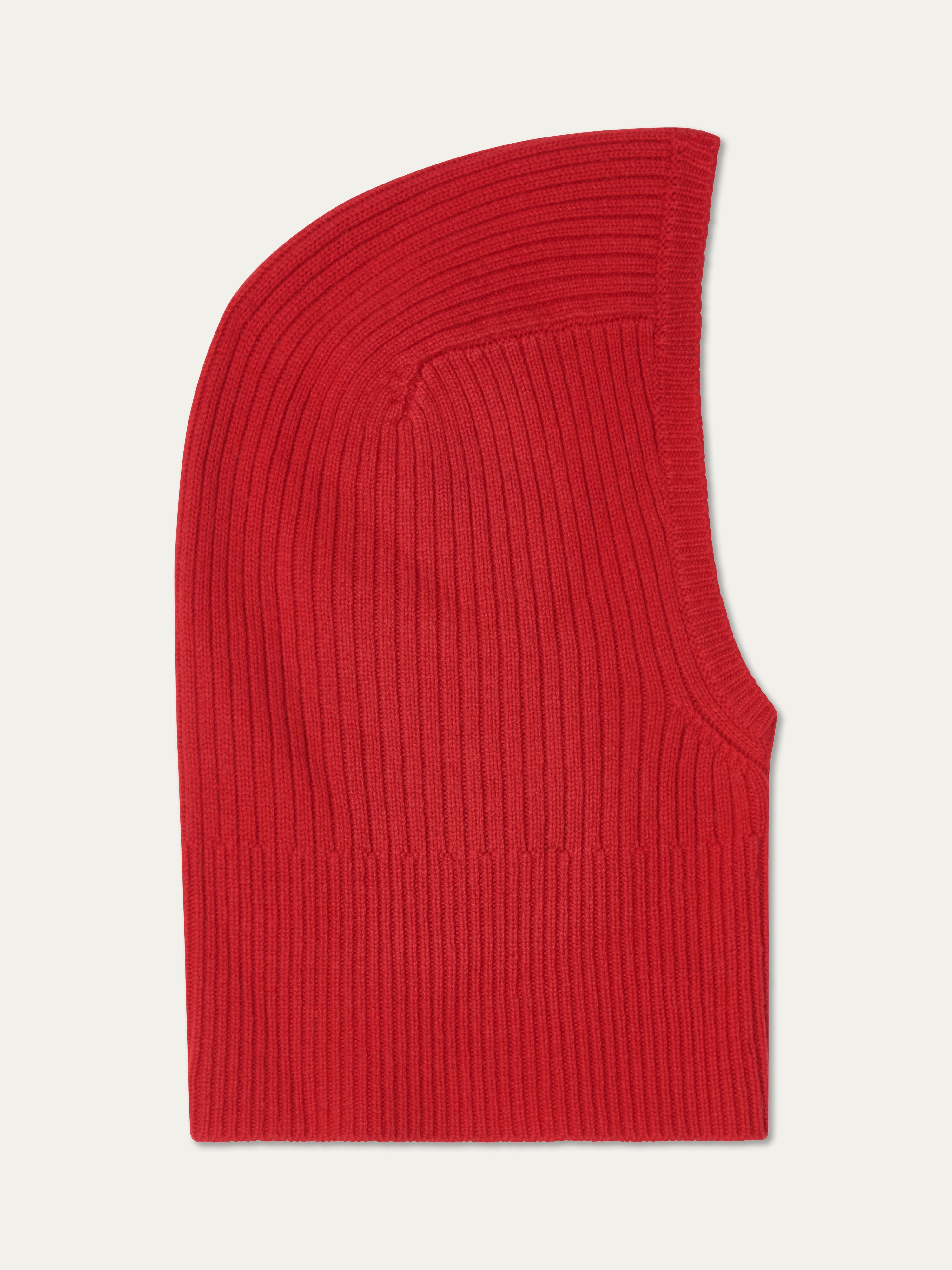 The Dal Balaclava by We Norwegians, in red ribbed Merino wool, features a snug, fitted design with a curved top and face opening. Inspired by classic Scandinavian winter wear, it’s shown lying flat on a white background.