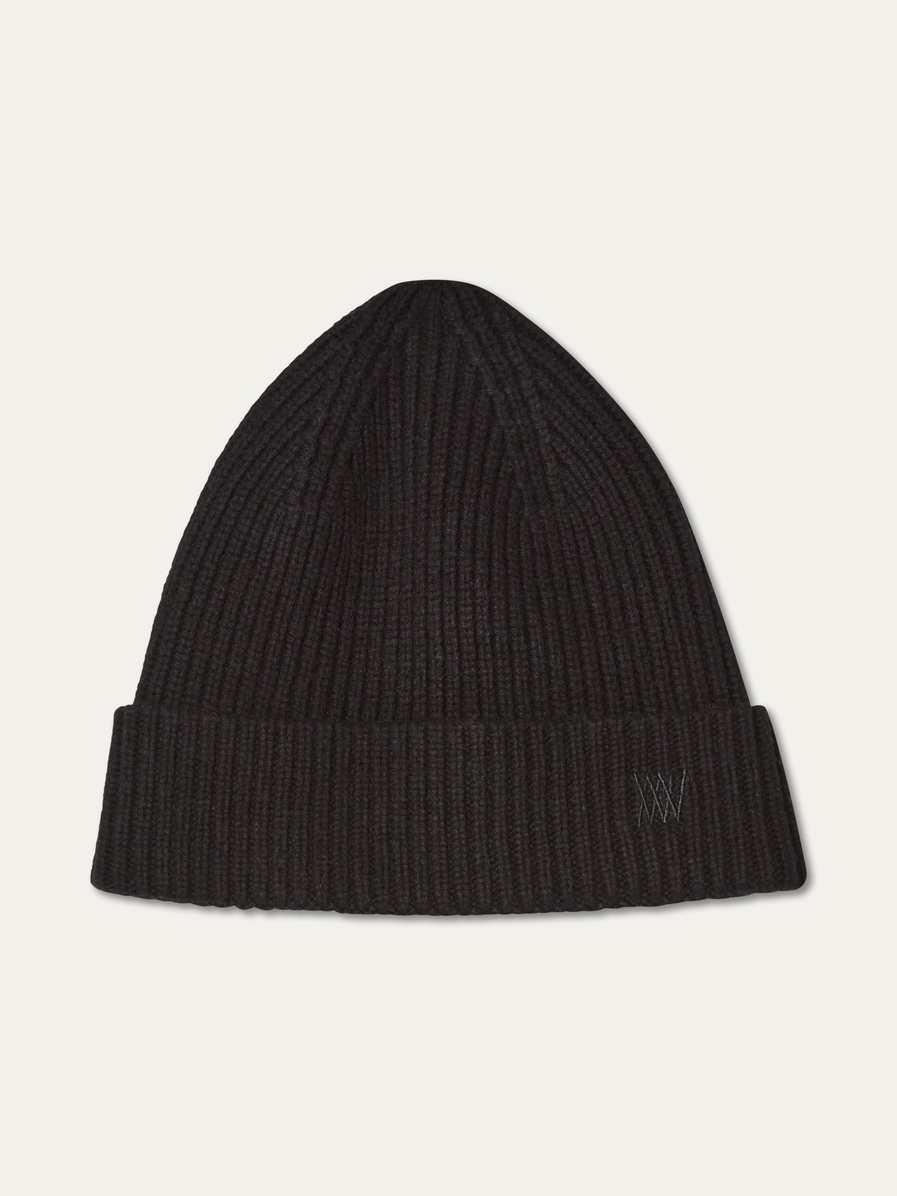 The Dal Hat by We Norwegians is a black ribbed knit beanie in Scandinavian style, featuring a folded brim and subtle embroidered initials at the bottom right, shown against a plain off-white background.