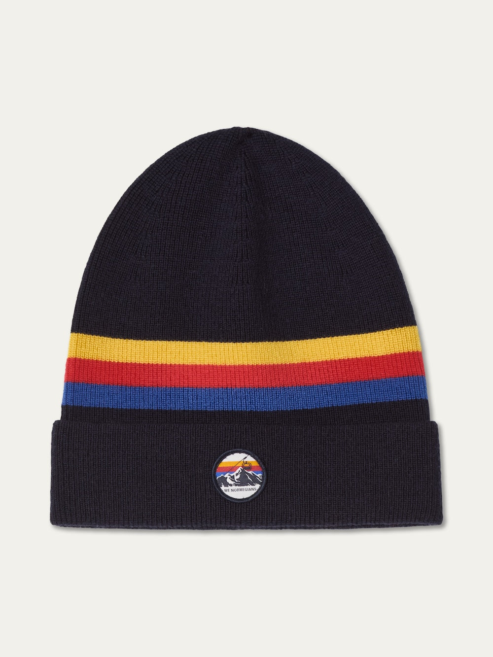 The We Norwegians FreeBird Hat is a dark knit hat with red, yellow, and blue horizontal rainbow stripes and a folded brim featuring a circular patch of a mountain scene beneath a colorful sky.