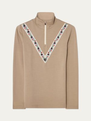 The We Norwegians WN x Markarian ZipUp women is a beige merino wool base layer with long sleeves, high collar, half-zip front, and V-shaped red, white, and black floral embroidery on the chest and shoulders.