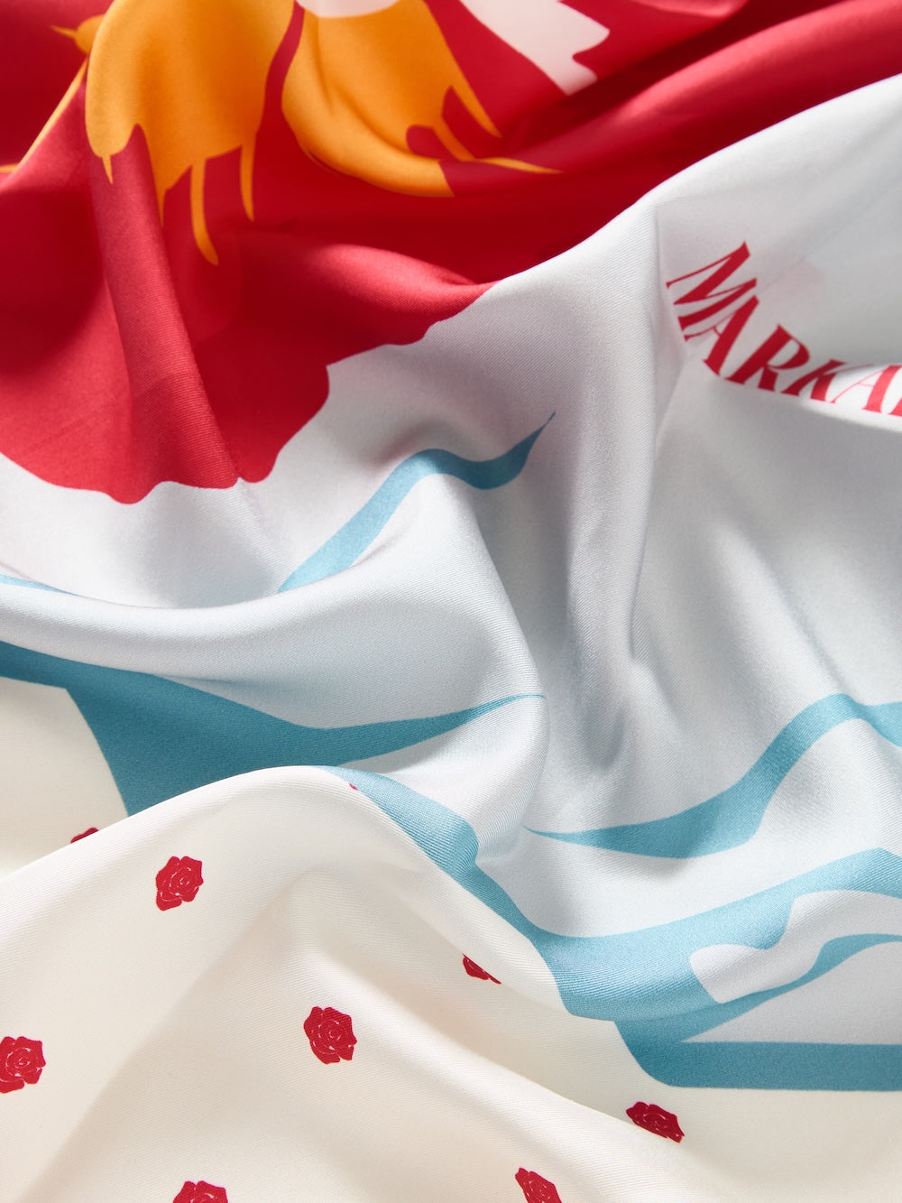 A close-up of the WN x Markarian Silk Scarf women by We Norwegians highlights its colorful red, yellow, and blue floral patterns with flowing lines, softly folded and creased.