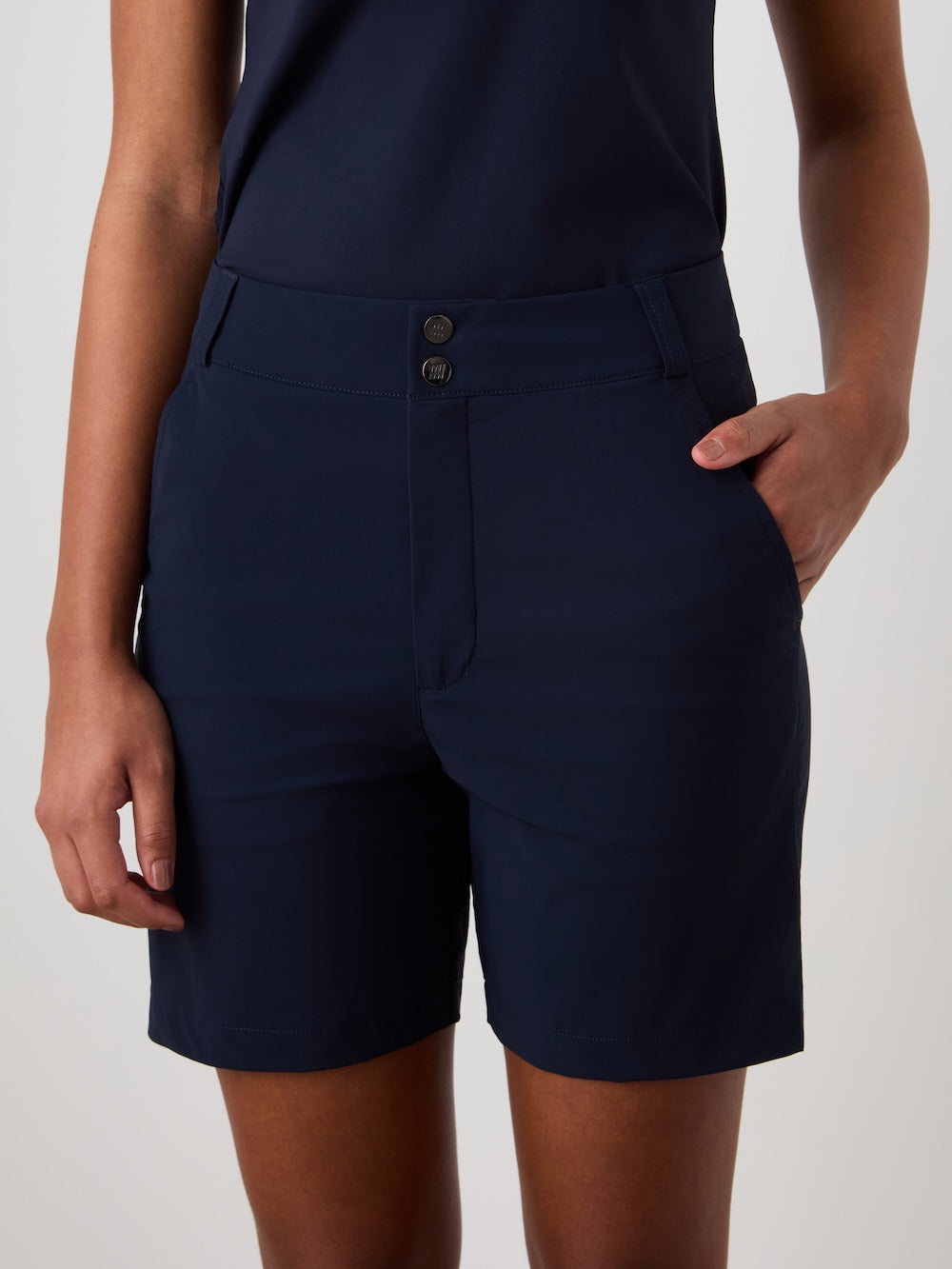 A person stands against a plain light background wearing We Norwegians Albatross Shorts Women in dark navy, made from 4-way stretch, water-repellent fabric, paired with a matching top; one hand is in their pocket, the other arm relaxed.