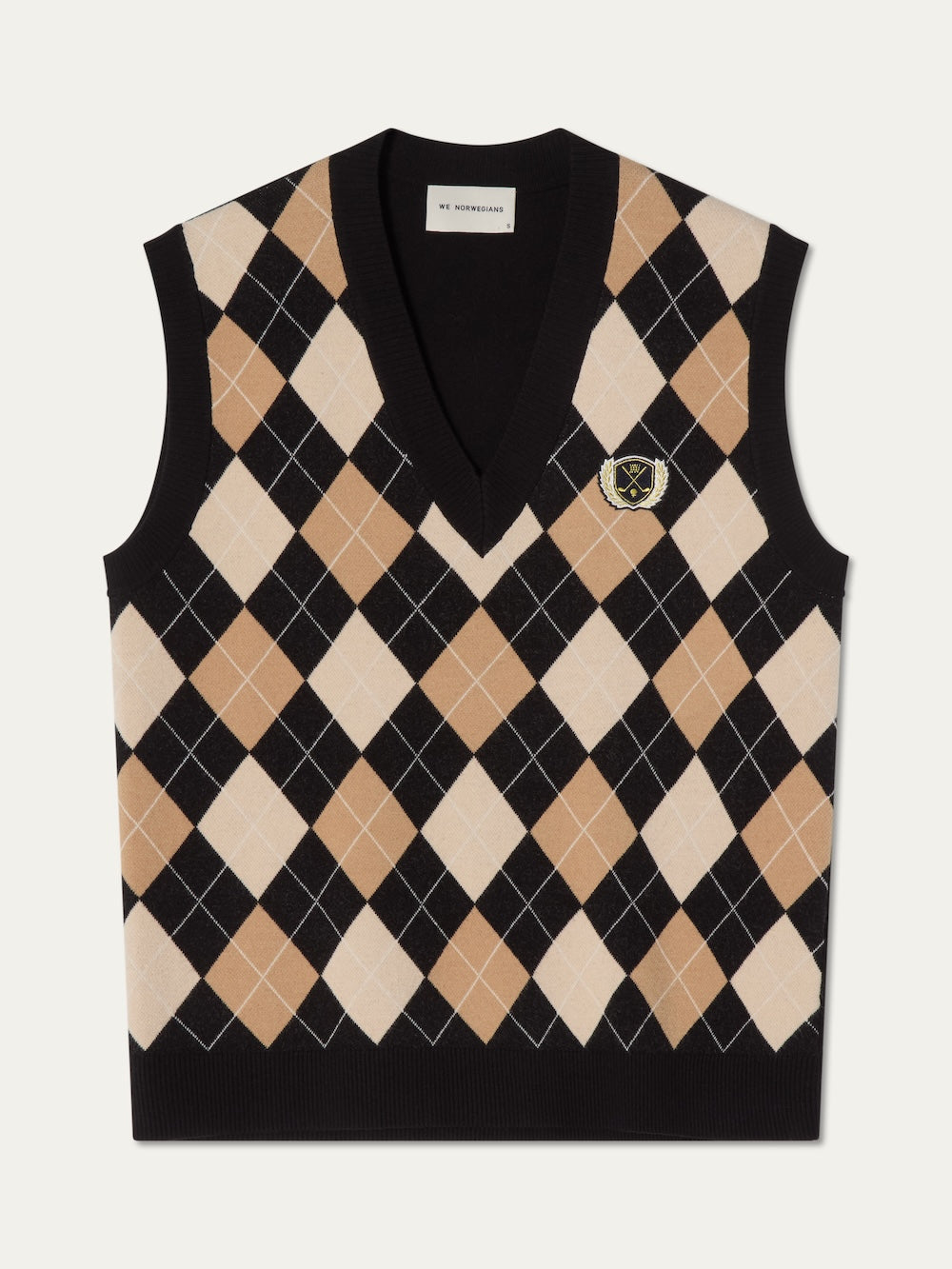 The We Norwegians Fairway Vest Women is a sleeveless argyle knit vest with a deep V-neck, tan, black, and white pattern, plus an embroidered crest on the chest—ideal for classic golf style on or off the course.