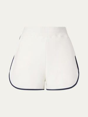 The We Norwegians Bounce Shorts Women are white, high-waisted retro tennis shorts with a wide elastic waistband and black piping, crafted from cotton sweatshirt fabric and shown from the back against a light background.