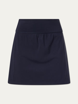 The We Norwegians Honor Skirt Women is a dark navy tennis skirt featuring a wide waistband, built-in shorts, and a sleek design, shown against a plain white background.