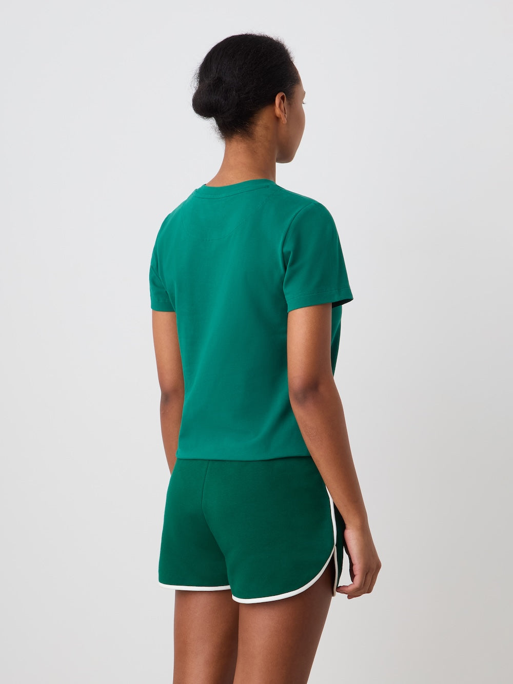 A person with short hair faces away, wearing the We Norwegians Love Tee Women—green with green shorts trimmed in white—for a look inspired by vintage tennis posters, set against a simple light background.