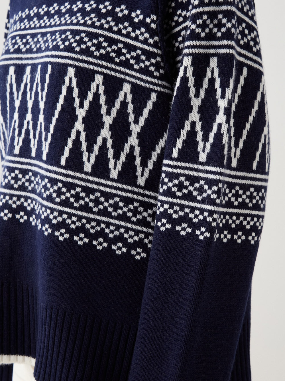 A close-up of the We Norwegians Setesdal Pullover for women, a navy blue knit sweater with white Nordic-inspired geometric patterns and ribbed edges at the sleeves and hem.