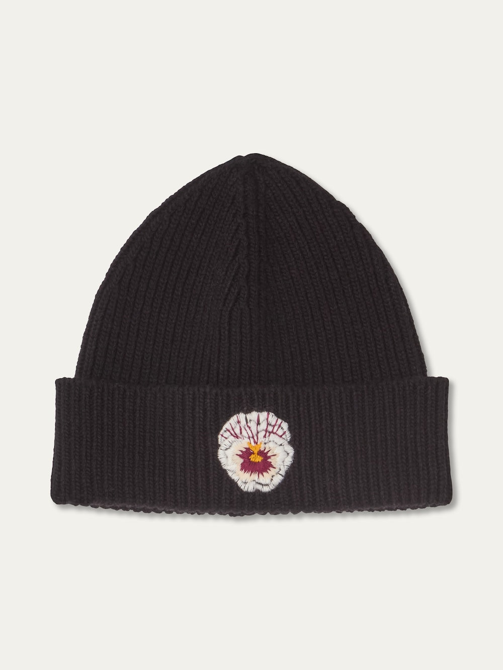 The WN x Markarian Hat Women by We Norwegians is a limited-edition black ribbed knit beanie with a folded brim, featuring an embroidered white and purple flower with a yellow center on the front.
