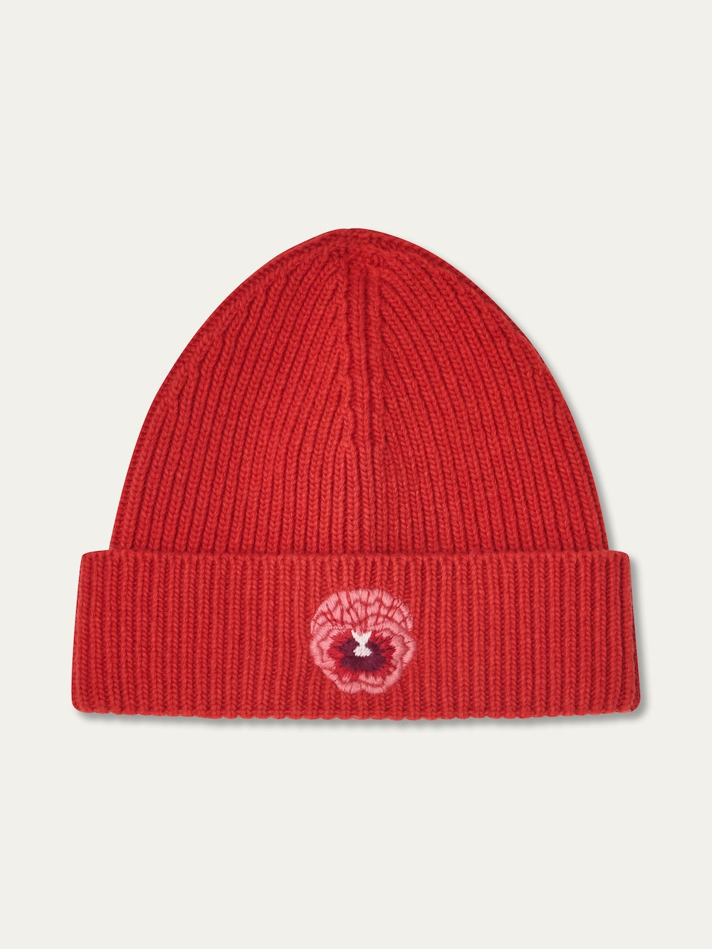 The WN x Markarian Hat Women by We Norwegians is a limited edition red ribbed knit beanie with a folded brim and an embroidered pink and white lion face patch on the front.