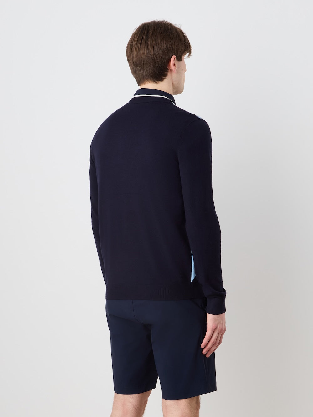 A man with short brown hair, seen from behind, models the We Norwegians Fairway Sweater Men—a navy long-sleeve polo shirt with matching shorts—styled for a sporty golf look against a plain light background.