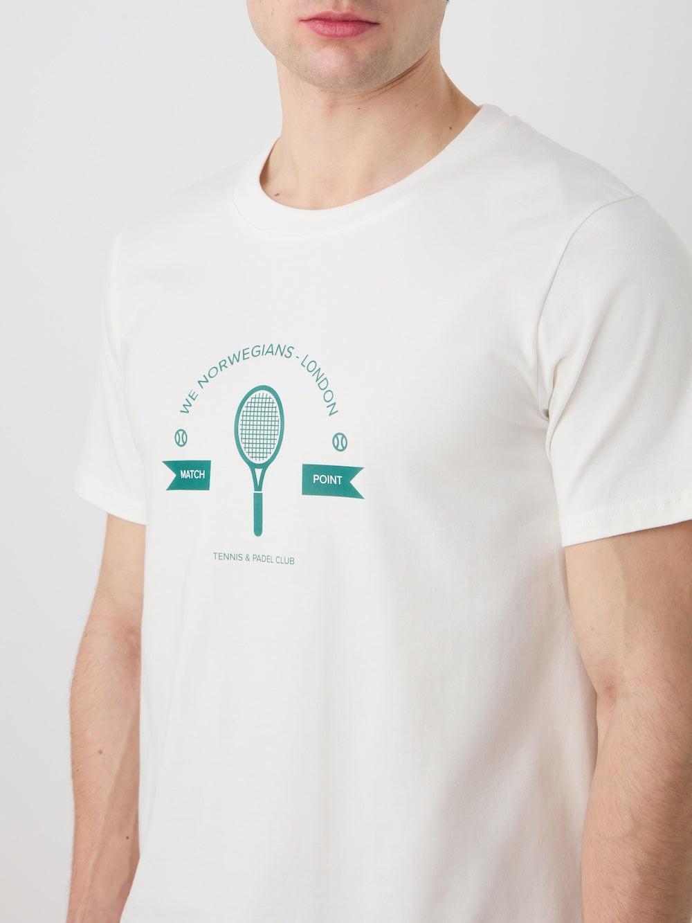 A man sports the Love Tee Men by We Norwegians—white cotton, green tennis racket and ball graphic, and retro text including "We Norwegians, London," "Match," "Point," and "Tennis & Padel Club.