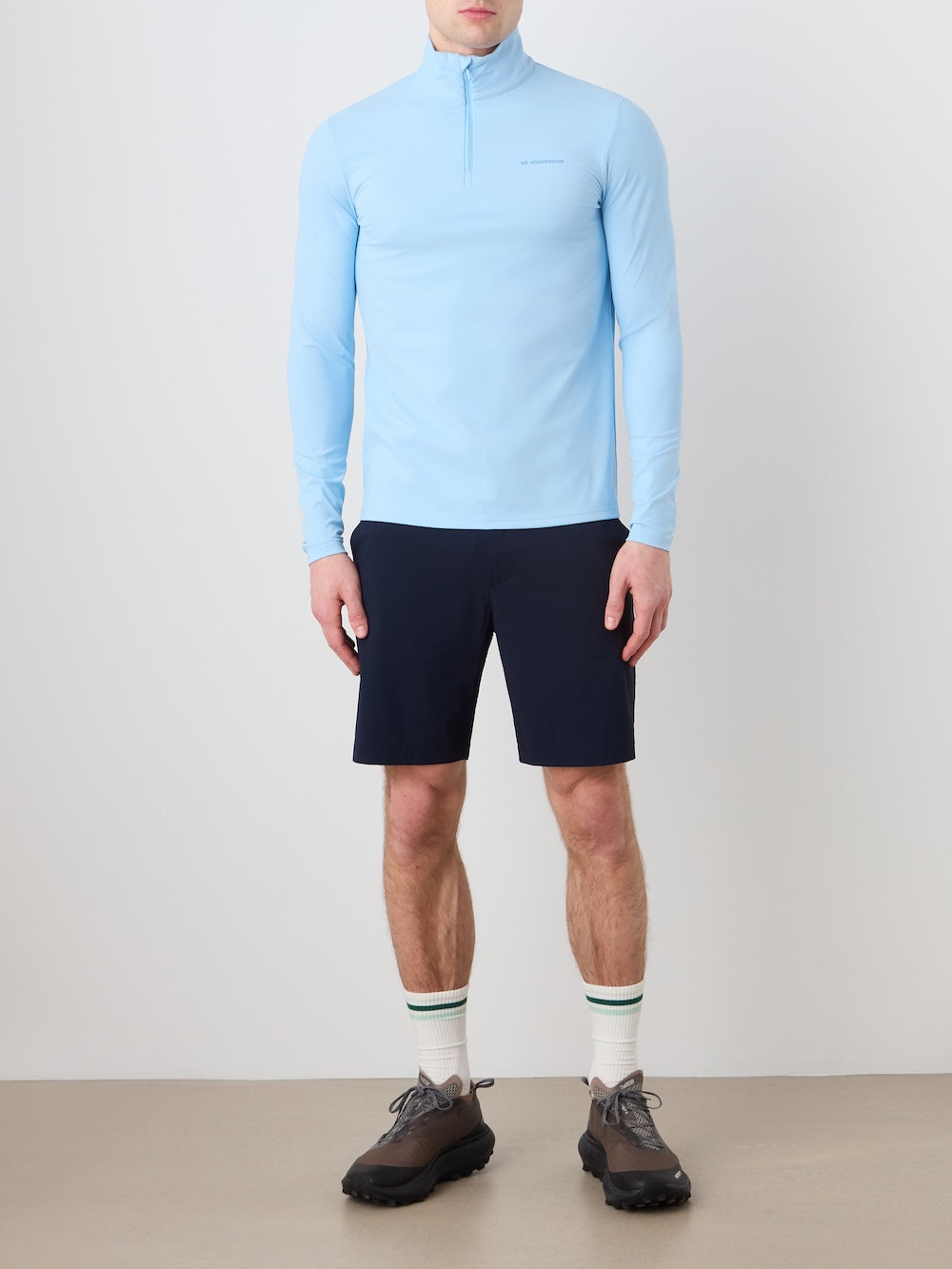 Person wearing a light blue long-sleeve shirt, navy shorts, and white socks with a green stripe on a plain background.