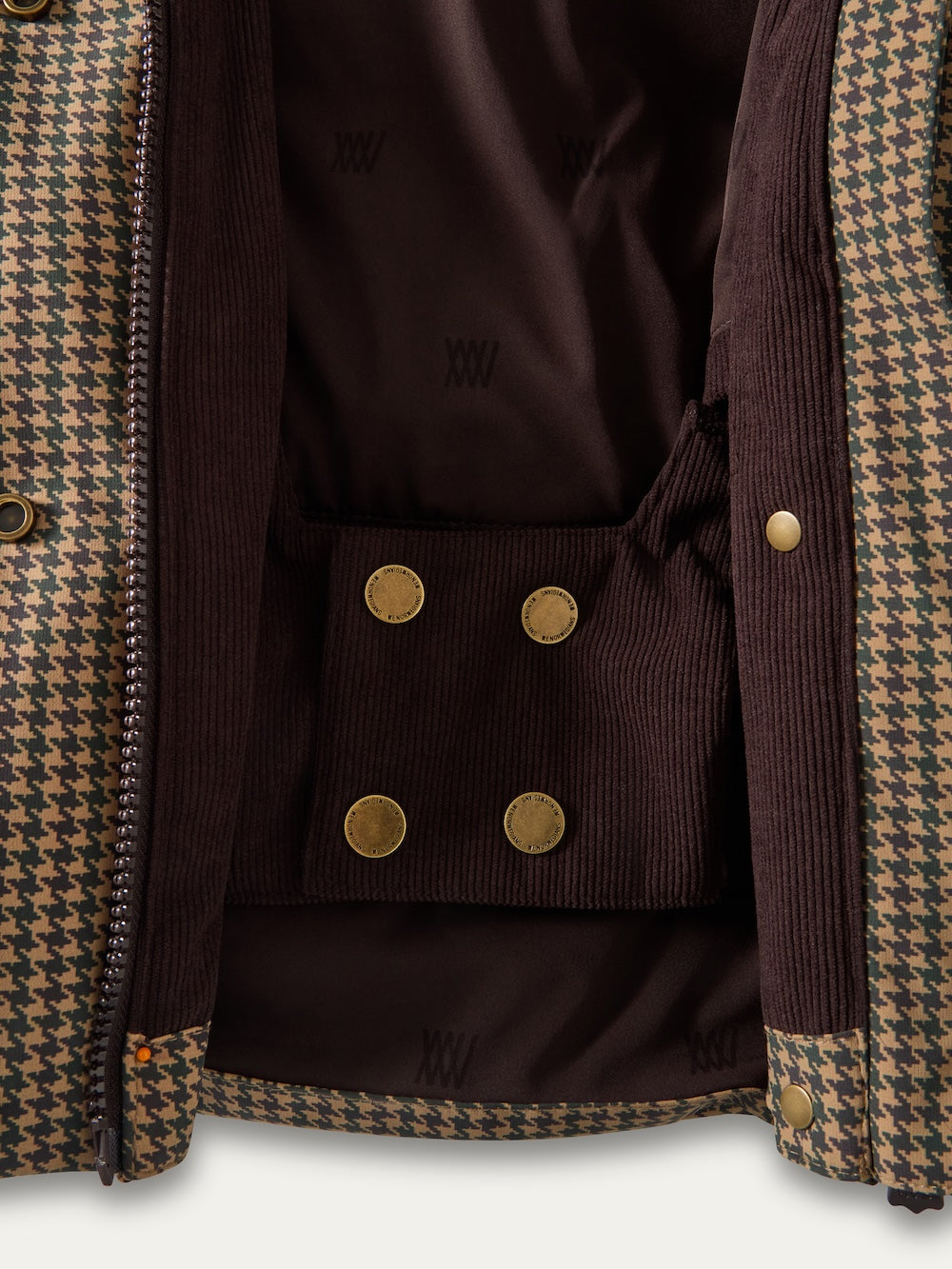 Close-up of the inside of the Glenshee Ski Jacket Women by We Norwegians, showing a brown and tan houndstooth pattern, brown corduroy lining, and gold snap buttons.