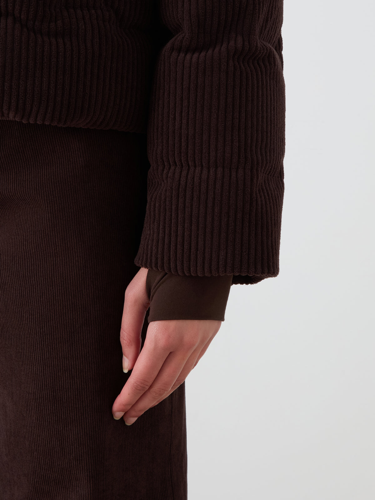 A person models the Britt Ski Jacket Women by We Norwegians in ribbed dark brown corduroy, standing against a plain white background with their arm relaxed at their side.