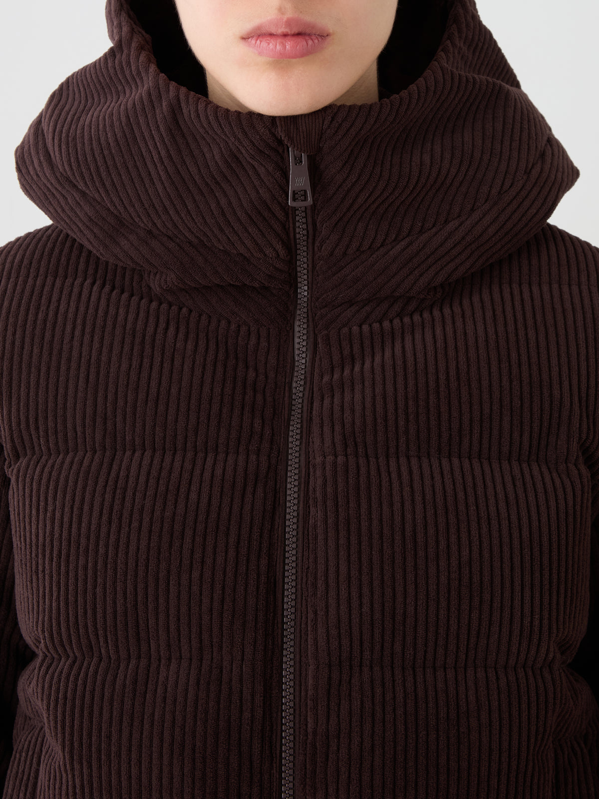 A person wearing the We Norwegians Britt Ski Jacket Women in brown corduroy with a large padded hood, zipped to the top and shown from the shoulders up, revealing only the lower part of their face.
