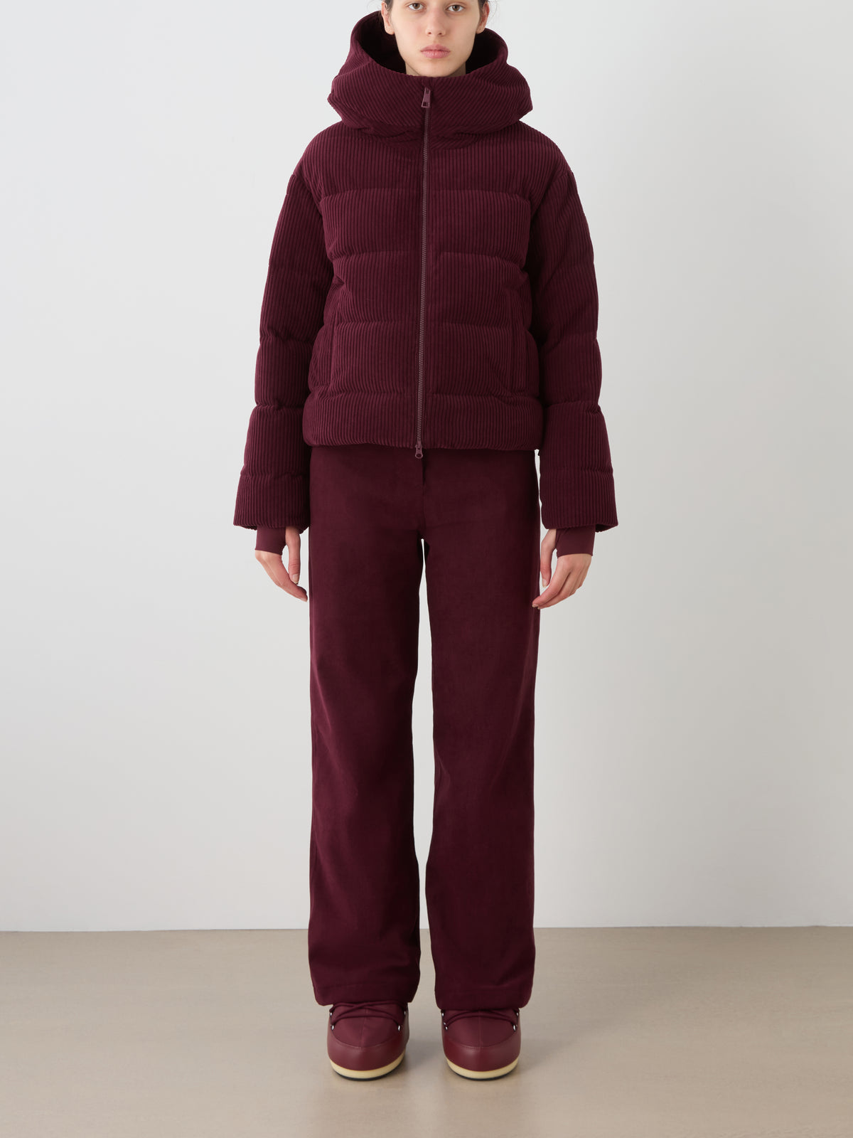A person stands against a plain background wearing the We Norwegians Britt Ski Jacket Women with matching wide-leg pants and burgundy shoes, creating a warm, cozy look ideal for sustainable ski wear fans.