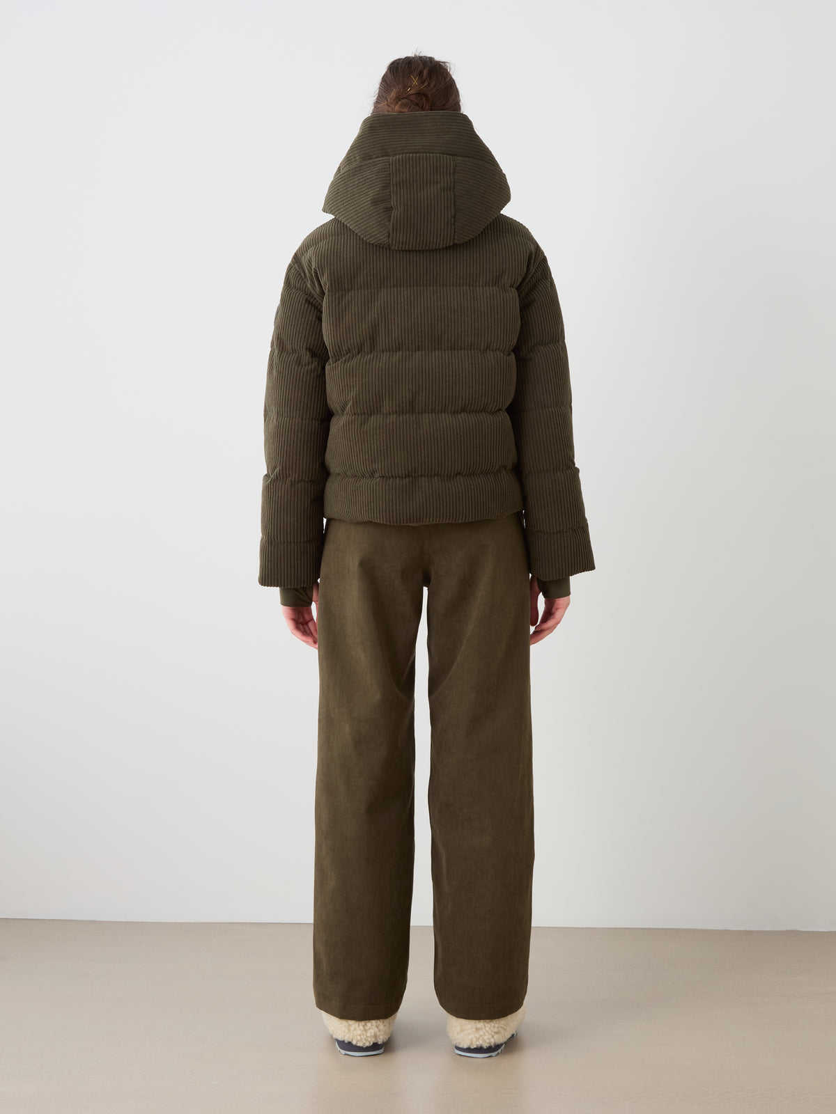 A person wears the We Norwegians Britt Ski Jacket Women in olive green with matching wide-leg pants, highlighting sustainable ski wear against a plain light background.