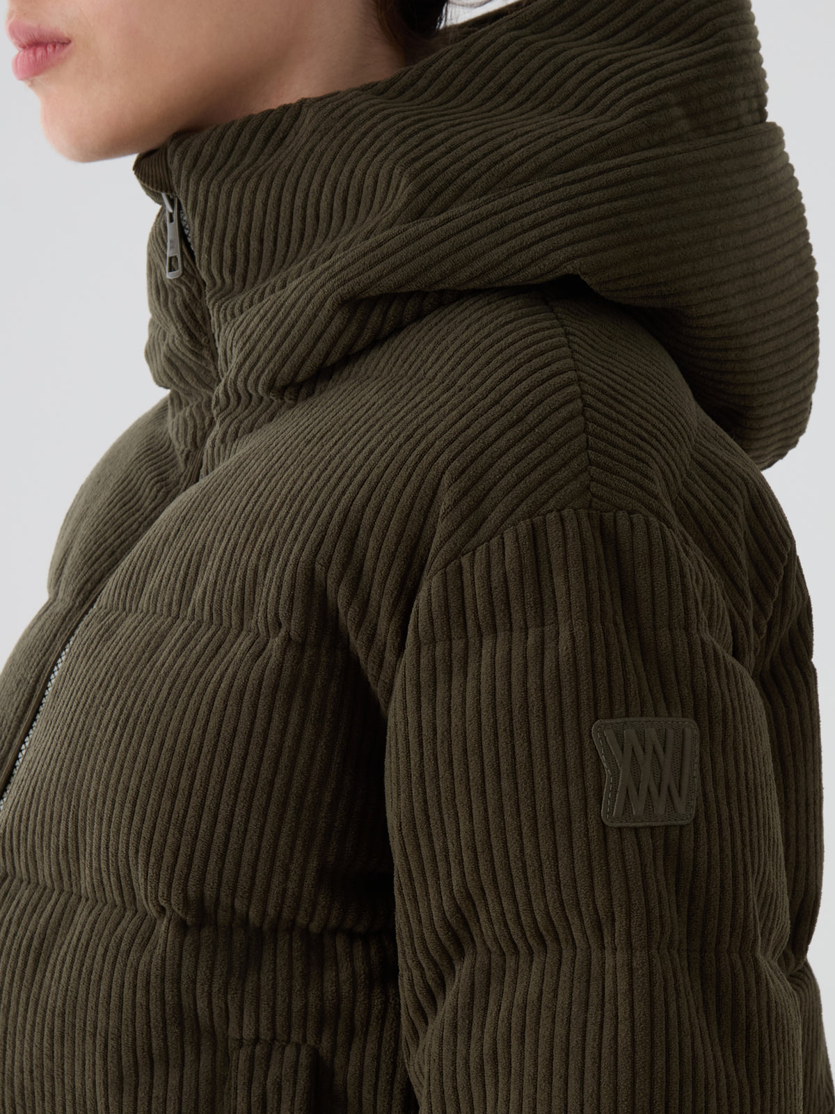Wearing the We Norwegians Britt Ski Jacket Women in olive green—a corduroy ski jacket featuring a hood, sleeve patch, and visible horizontal and vertical stitching.