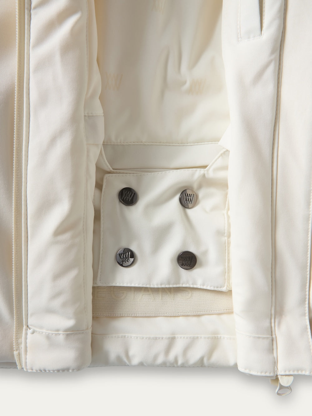Close-up of the inside of the Tyin Tailored Ski Jacket Women by We Norwegians, featuring a snap button pocket with four black buttons and subtle stitching on the cream-colored lining.