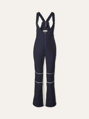 The Solo Bib Pant Women by We Norwegians features navy blue fabric with white piping, a front zipper, flared legs, adjustable straps, and a fitted waist for vintage-inspired alpine style on or off the slopes.