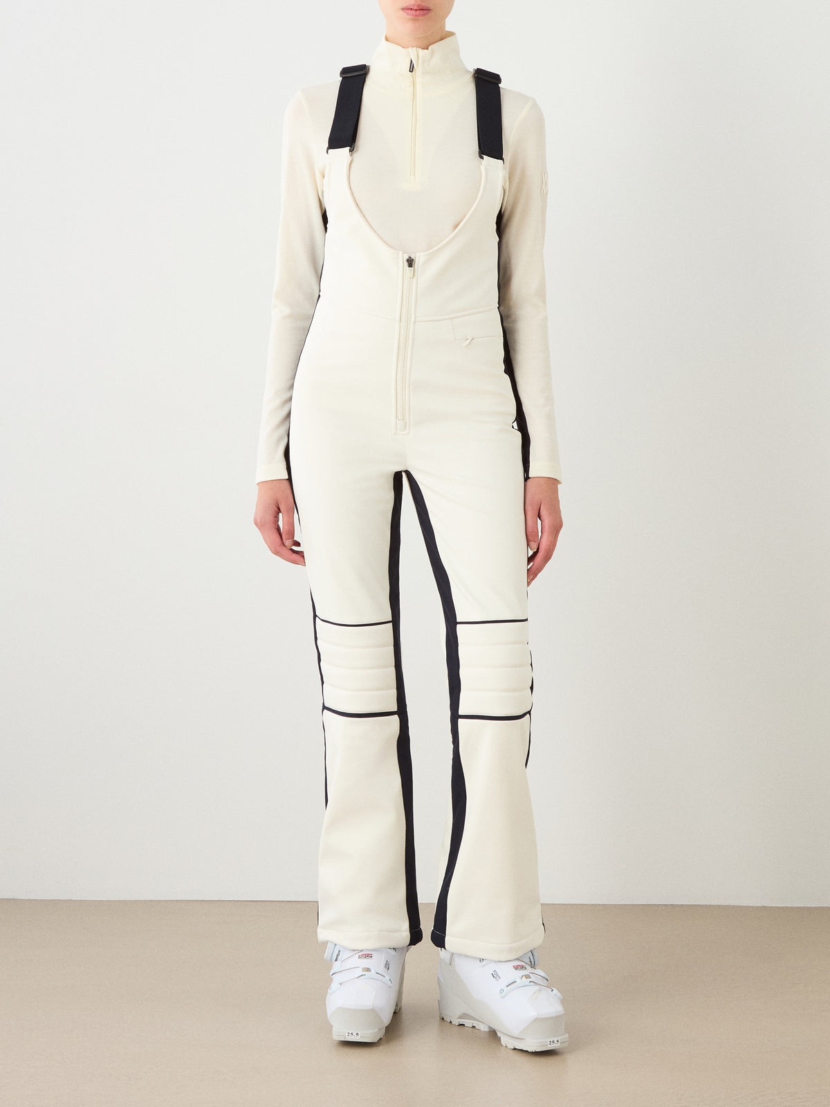 Wearing the We Norwegians Solo Bib Pant Women, this look channels vintage alpine ski style with cream and black details—perfect après-ski wear against a plain background.