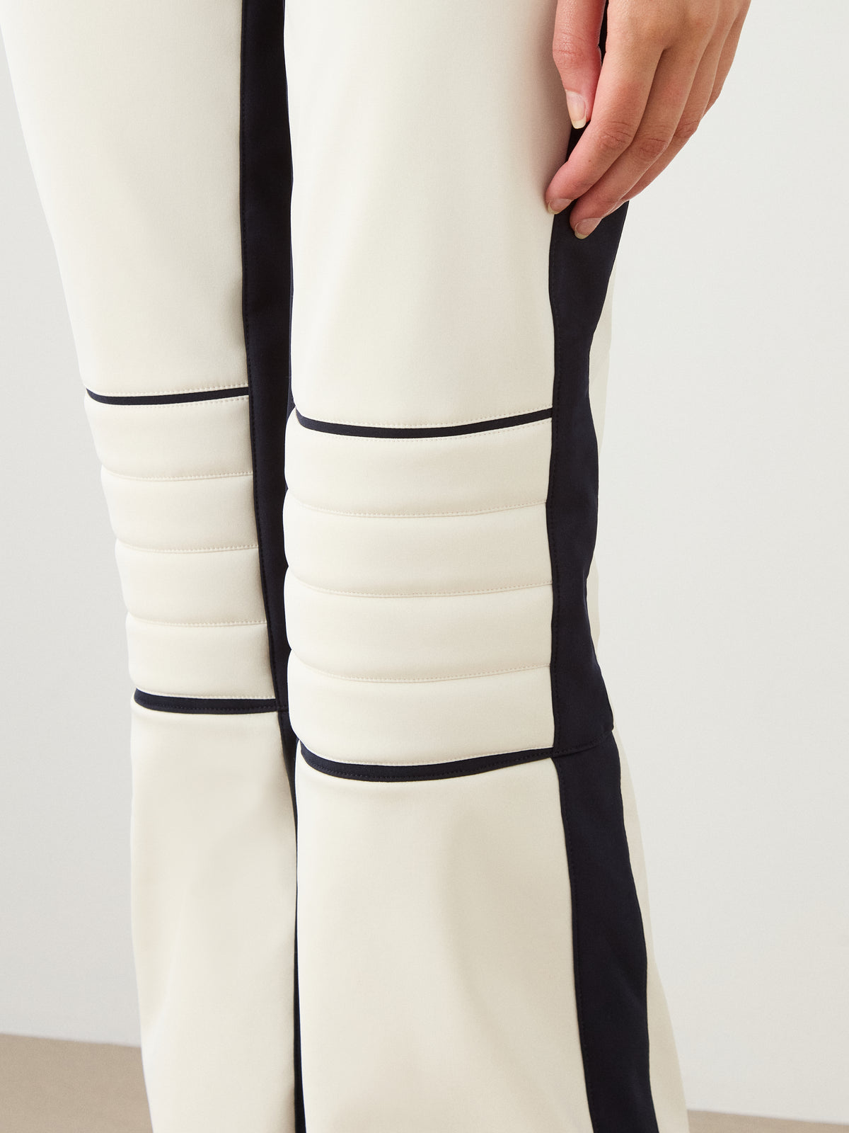 A close-up of a person wearing the We Norwegians Solo Bib Pant Women in cream with black stripes and ribbed knee details, showing off vintage alpine ski style.