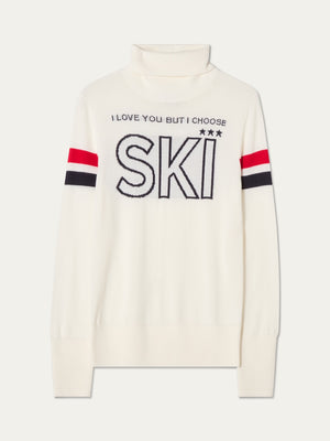 The We Norwegians Bibi Fitted Sweater Women is a white merino wool turtleneck featuring bold red and black sleeve stripes and “I LOVE YOU BUT I CHOOSE SKI ★★★” emblazoned across the chest, embodying the retro ski fashion aesthetic.