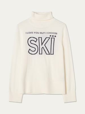 The Bibi Sweater Women by We Norwegians is a white turtleneck with ribbed cuffs and hem, inspired by retro ski fashion. It features black text on the front that reads, “I LOVE YOU BUT I CHOOSE SKI,” with three stars above the word “SKI.”.