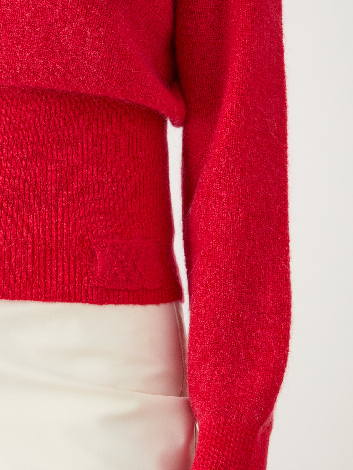 A person wearing the We Norwegians Pudder Sweater Women in bright red, paired with a cream-colored skirt, pictured from the shoulders to the hips.
