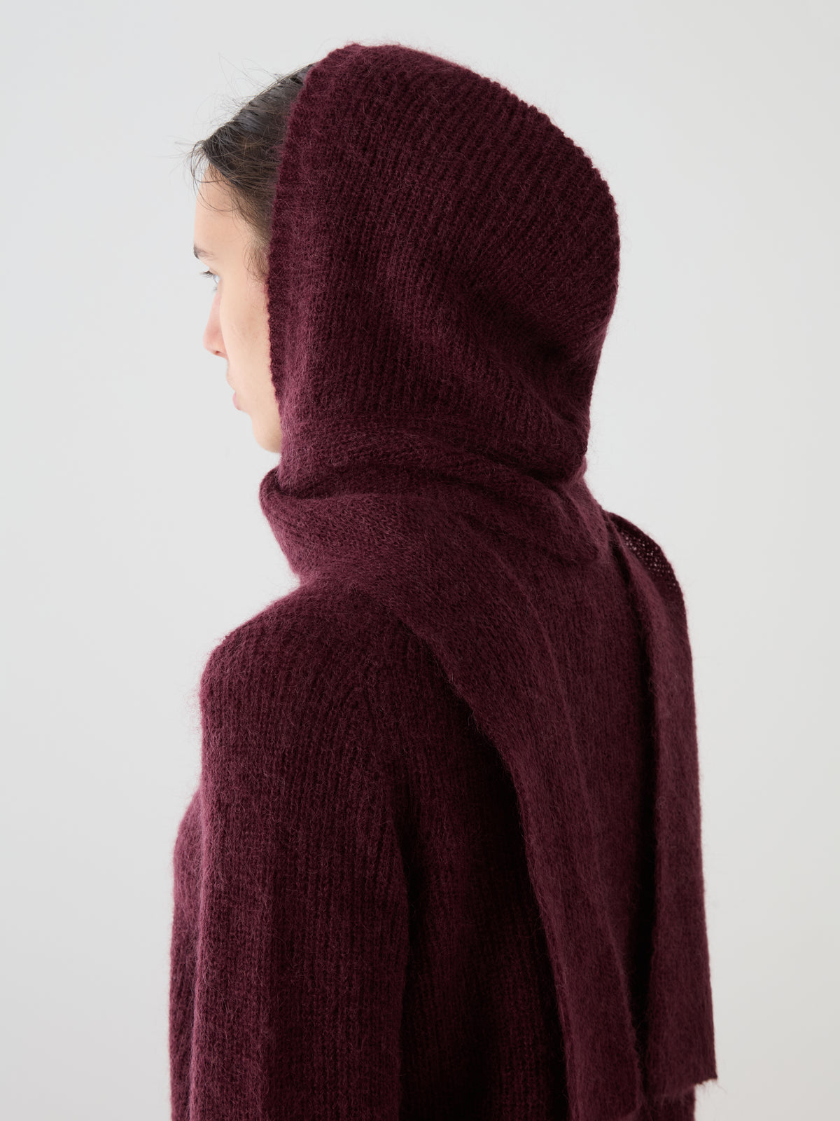 Profile view of a person wearing a cosy, fuzzy dark burgundy We Norwegians Pudder Balaclava.
