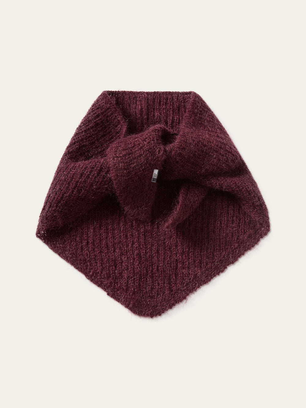 A luxurious Pudder Scarf by We Norwegians is displayed folded flat on a white surface, showcasing its rich burgundy knit texture, pointed end, and invitingly soft feel—a refined designer winter accessory that brings warmth and sophistication to any outfit.