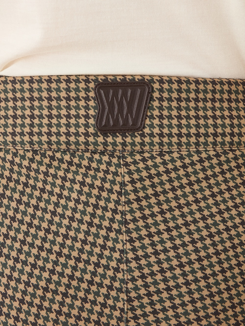 Close-up of the back waistband of the Glenshee Ski Pant Women by We Norwegians, showing its houndstooth pattern and black leather patch with geometric stitching, styled with a cream top.