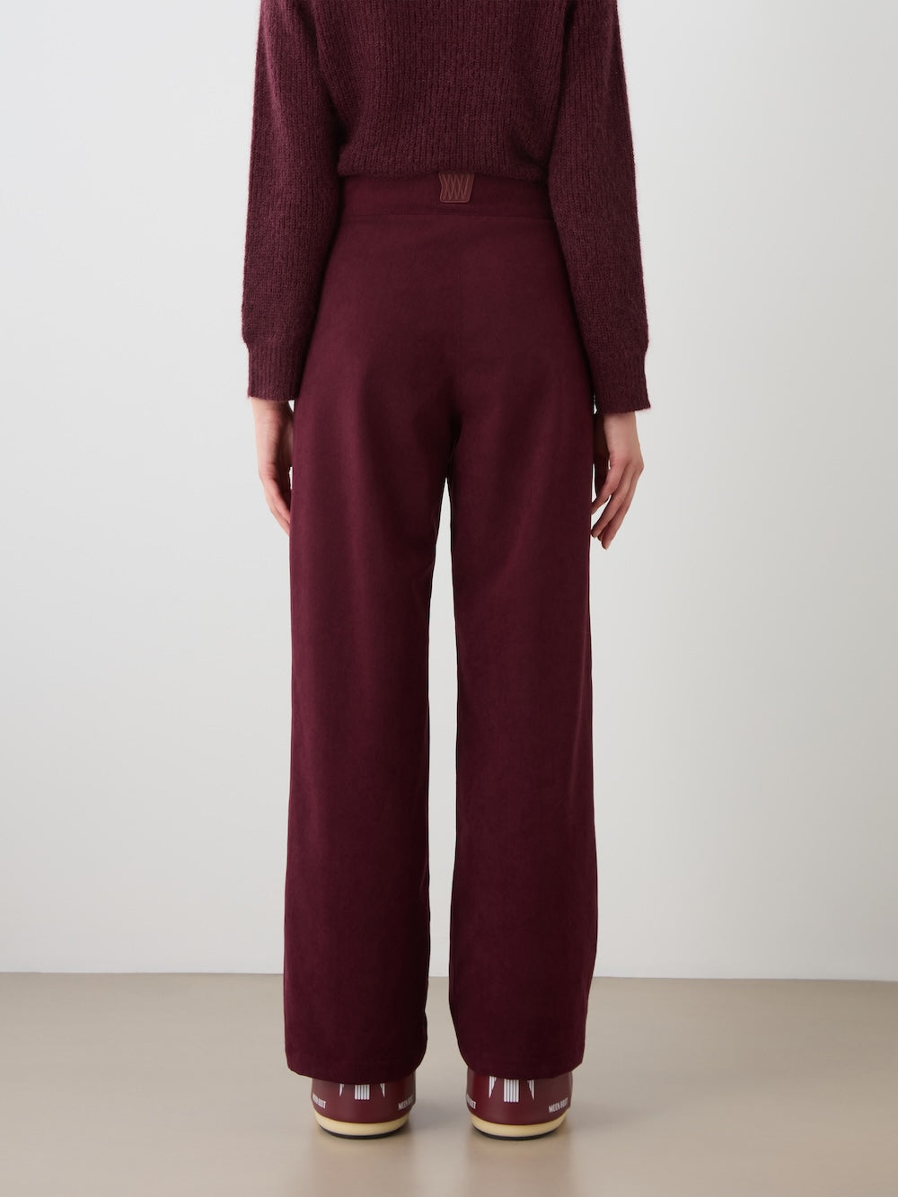 A person wearing the We Norwegians Britt Palazzo Ski Pant for women, paired with a matching burgundy sweater, stands facing away from the camera against a plain background.