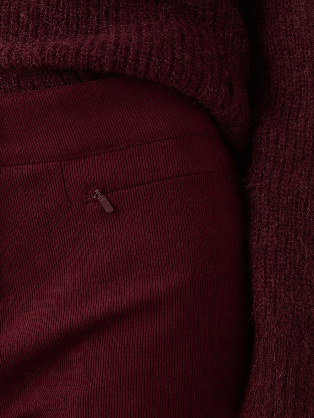 Close-up of a person wearing a textured dark burgundy sweater and the We Norwegians Britt Palazzo Ski Pant Women, featuring a high waist and visible zipper pocket.