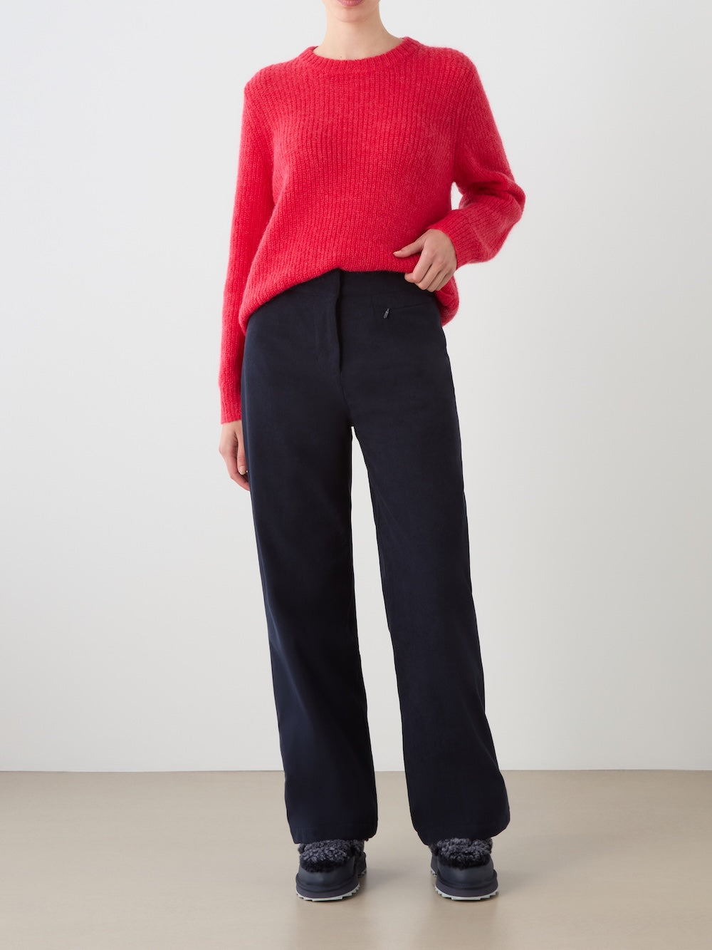 A person wearing the We Norwegians Britt Palazzo Ski Pant for women in dark navy, paired with a bright red sweater and black shoes, stands against a plain light background. Their face is not visible.