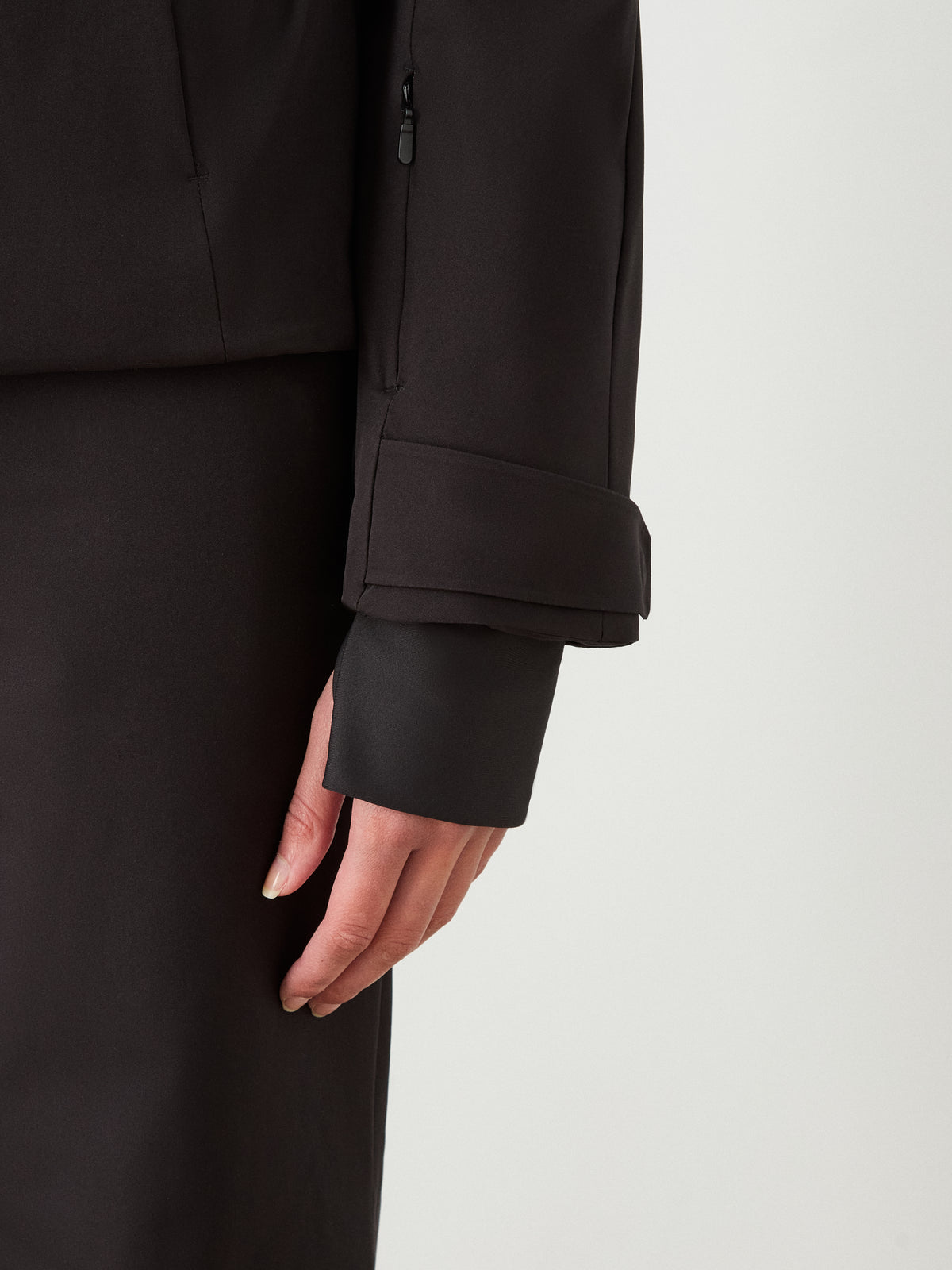 A close-up of a person’s left hand by their side, wearing the We Norwegians Finse Ski Jacket Women, featuring an adjustable cuff strap. The background is plain and light-colored.