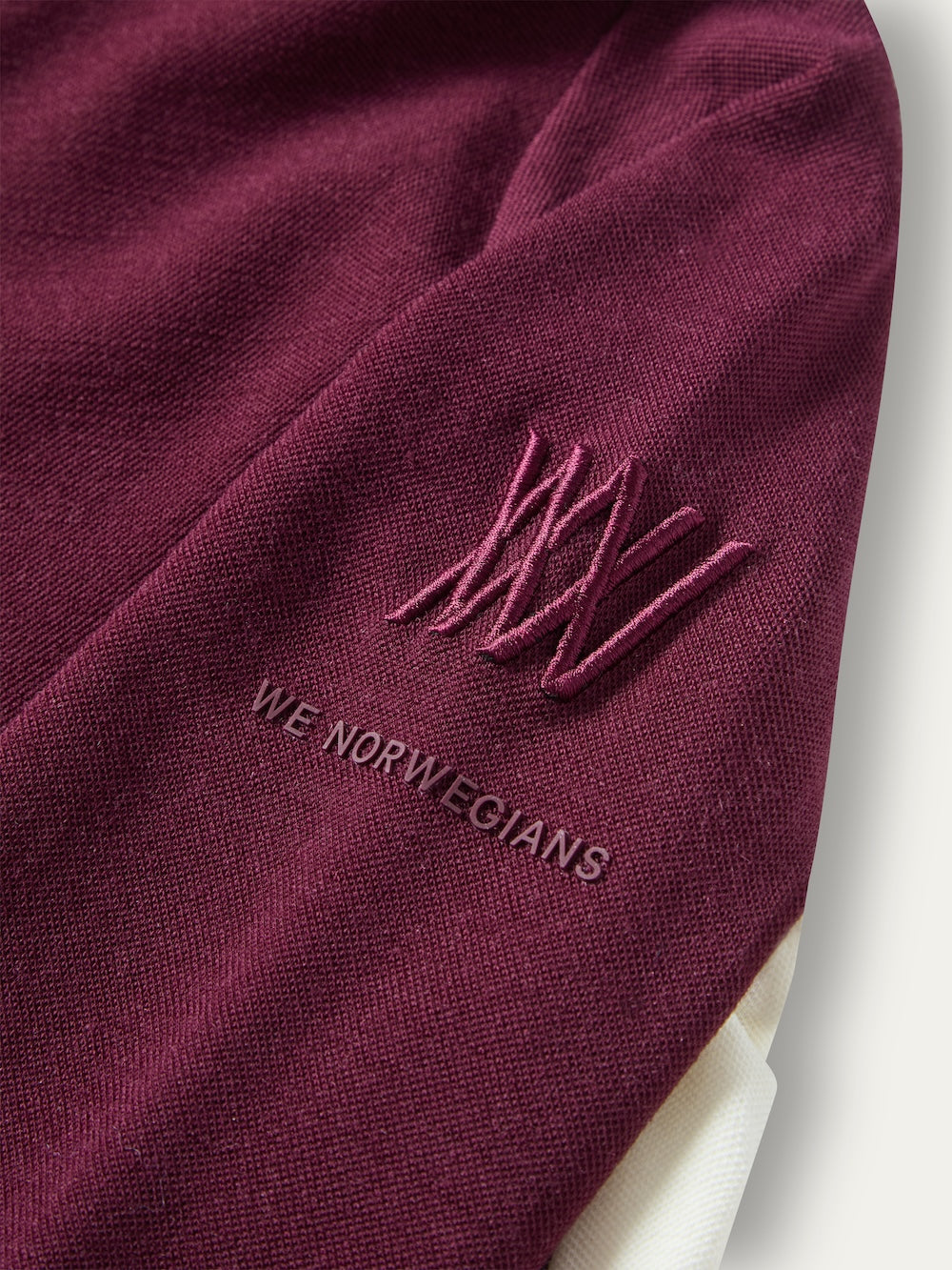 Close-up of a deep maroon We Norwegians Voss ZipUp Women sleeve featuring an embroidered logo and the brand name in dark lettering.