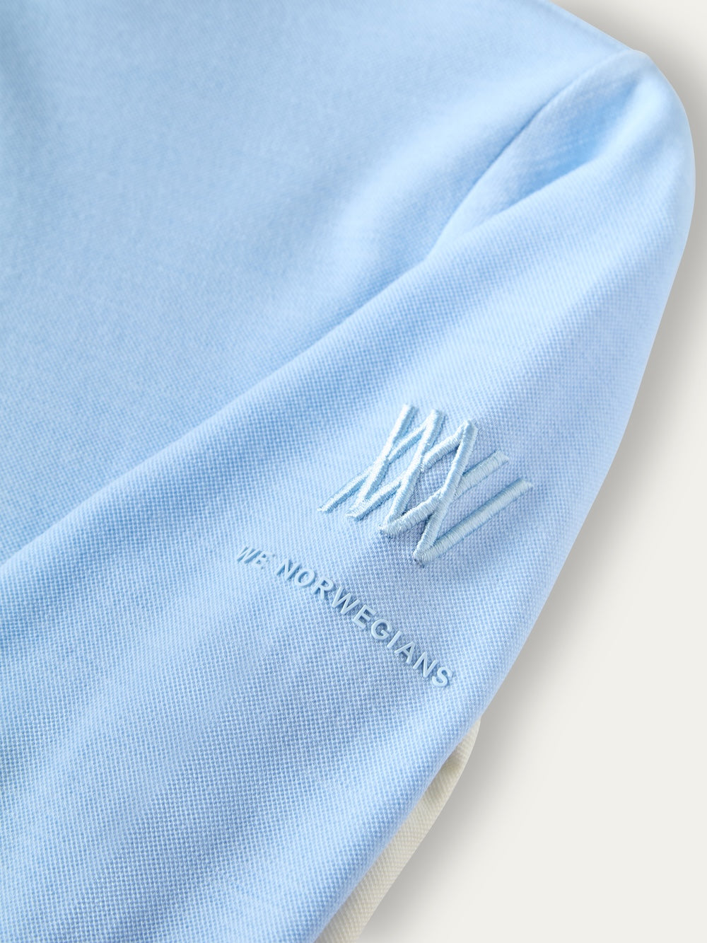Close-up of a light blue We Norwegians Voss ZipUp Women base layer, featuring an embroidered logo and the brand name on the sleeve.