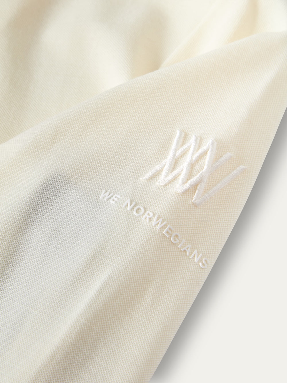 Close-up of a white We Norwegians Voss ZipUp Women base layer featuring an embroidered logo and text on the sleeve.