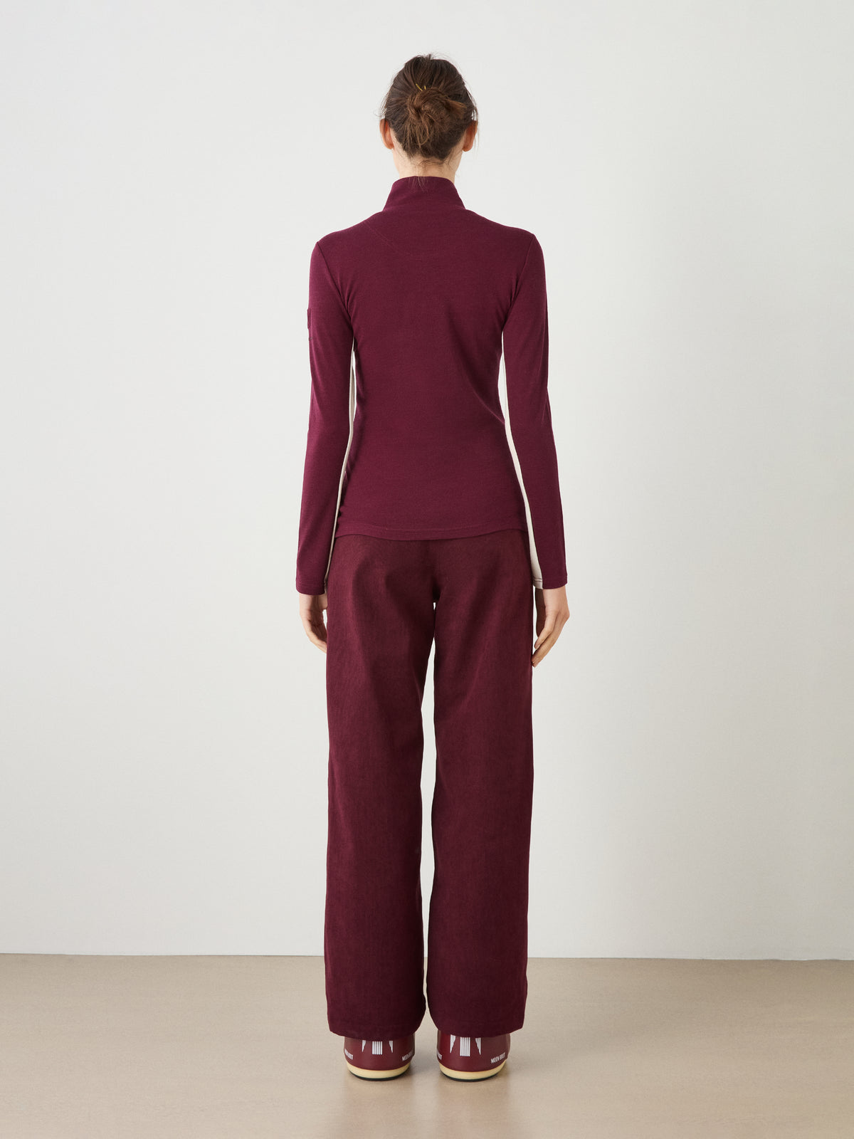 A person viewed from behind wearing a burgundy We Norwegians Voss Chevron ZipUp Women with light-colored side panels and matching burgundy wide-leg trousers.