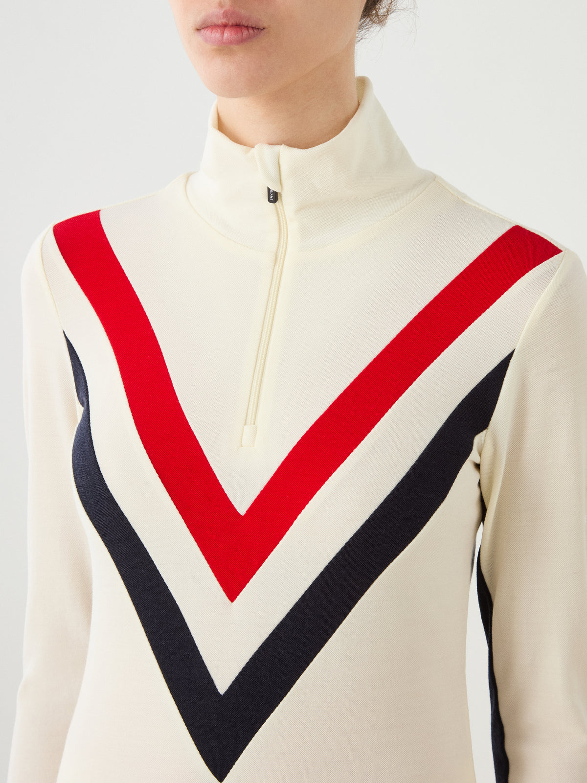 We Norwegians Voss Chevron ZipUp Women cream-colored Merino wool zip-up mock neck top featuring red and navy blue chevron stripes on the chest.