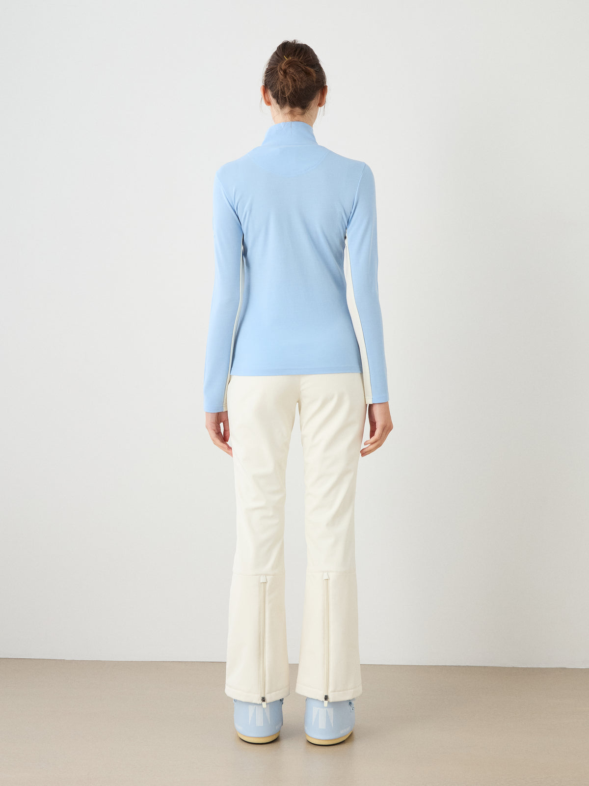 Back view of a person wearing a light blue We Norwegians Voss Chevron ZipUp Women and white trousers with zippered hems.