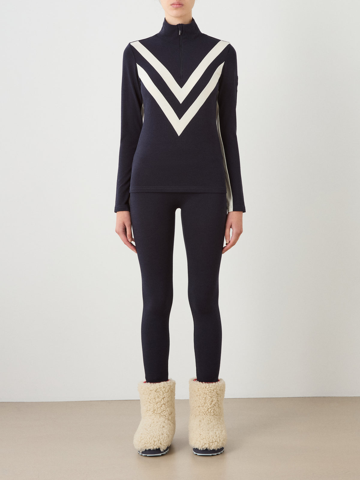 A navy We Norwegians Voss Chevron ZipUp Women top with white chevron stripes on the chest, matching navy leggings, and cream-colored fleece-lined boots.