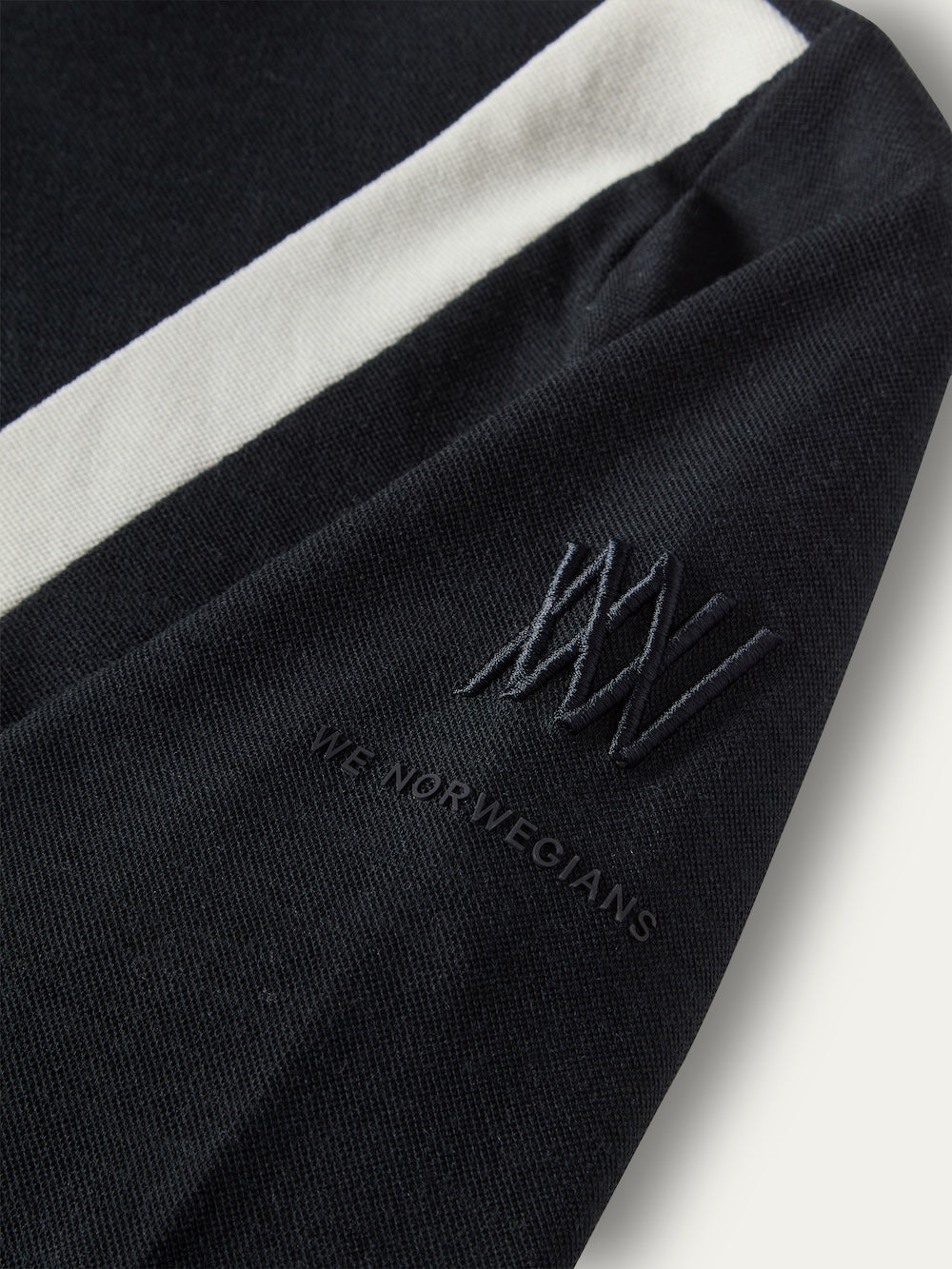 Black long-sleeved We Norwegians Voss Chevron ZipUp Women top in Merino wool, featuring a white stripe down the arm with an embroidered logo and text on the sleeve.
