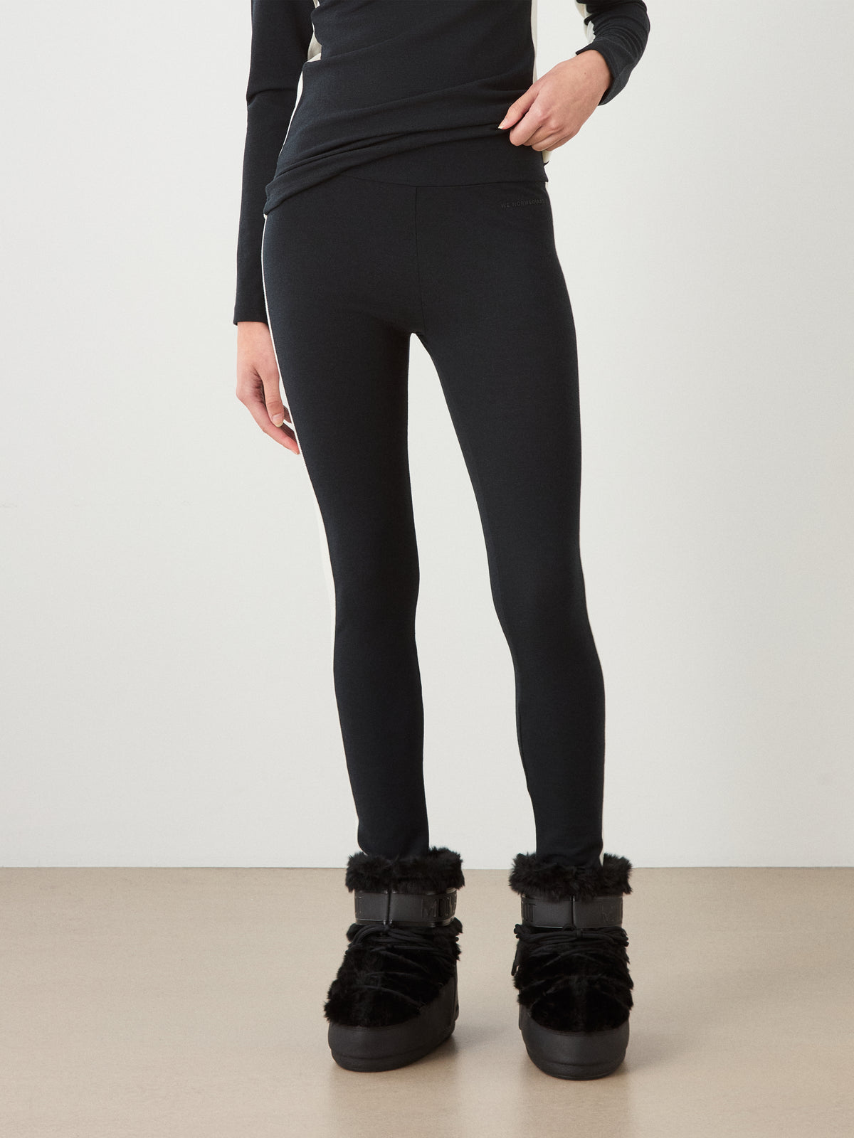 Person wearing Voss Leggings Women made of breathable merino wool with a white side stripe, paired with black fur-trimmed boots.