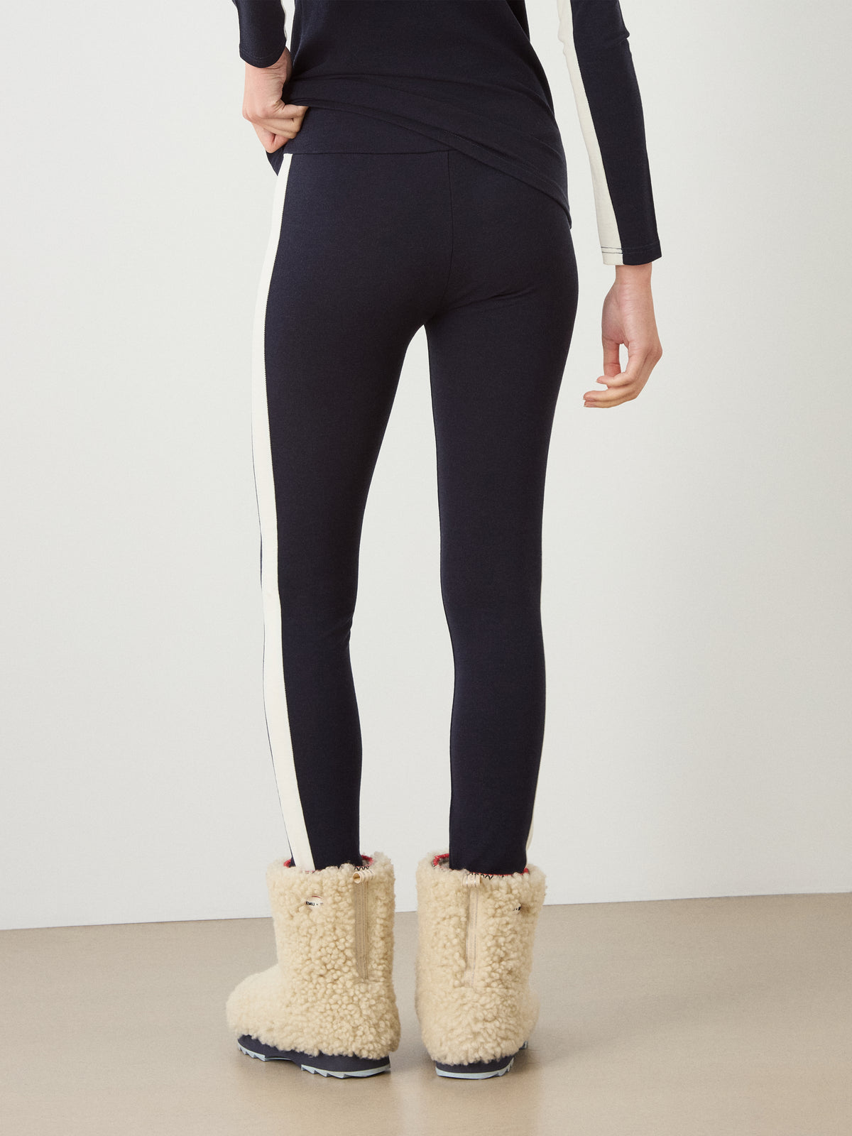 Back view of a person wearing dark, breathable Voss Leggings Women with a white side stripe and cream-colored fleece winter boots.