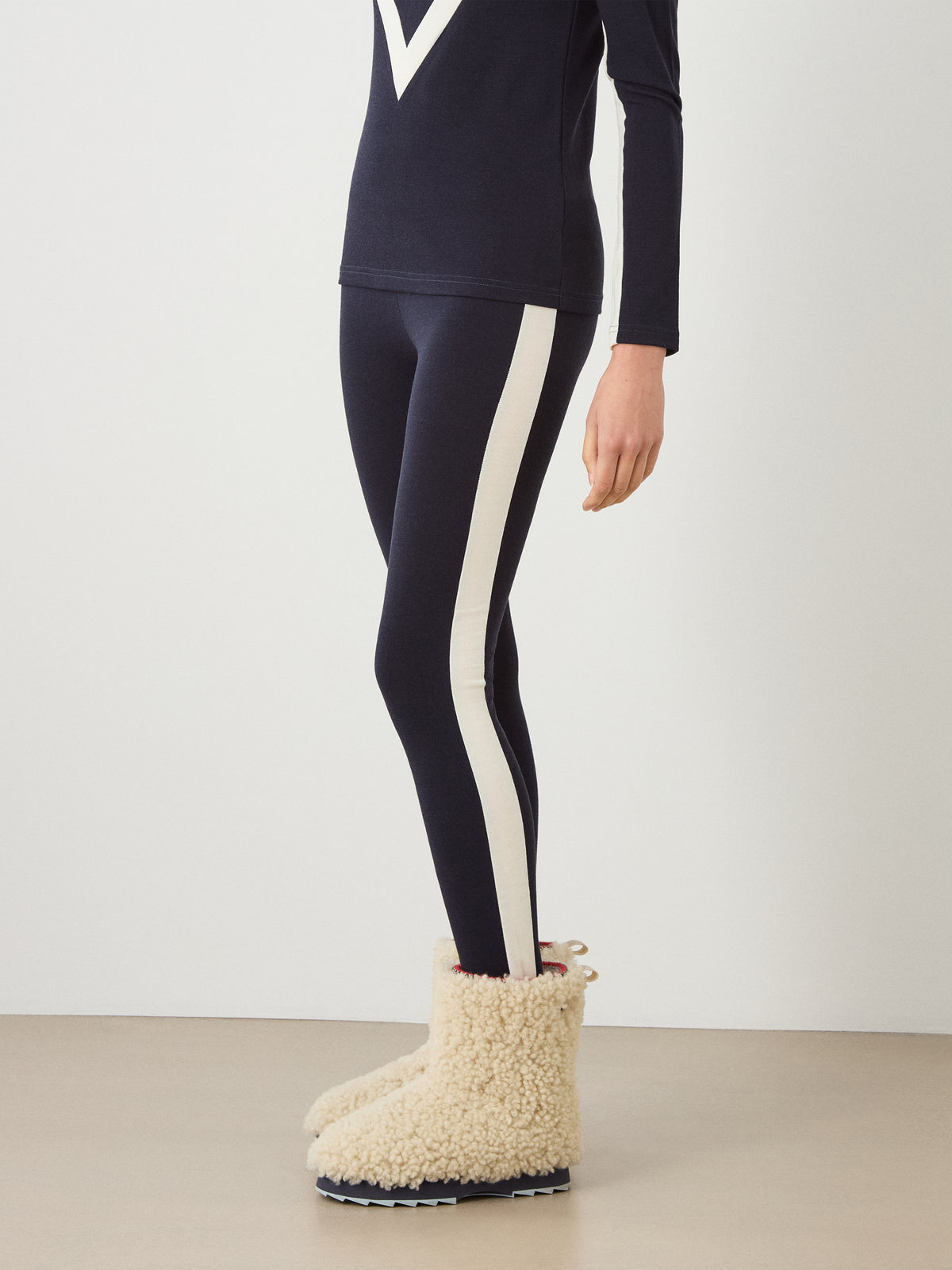 Side view of navy Voss Leggings Women with a wide white stripe down the side, worn with cream-colored fleece-lined boots.